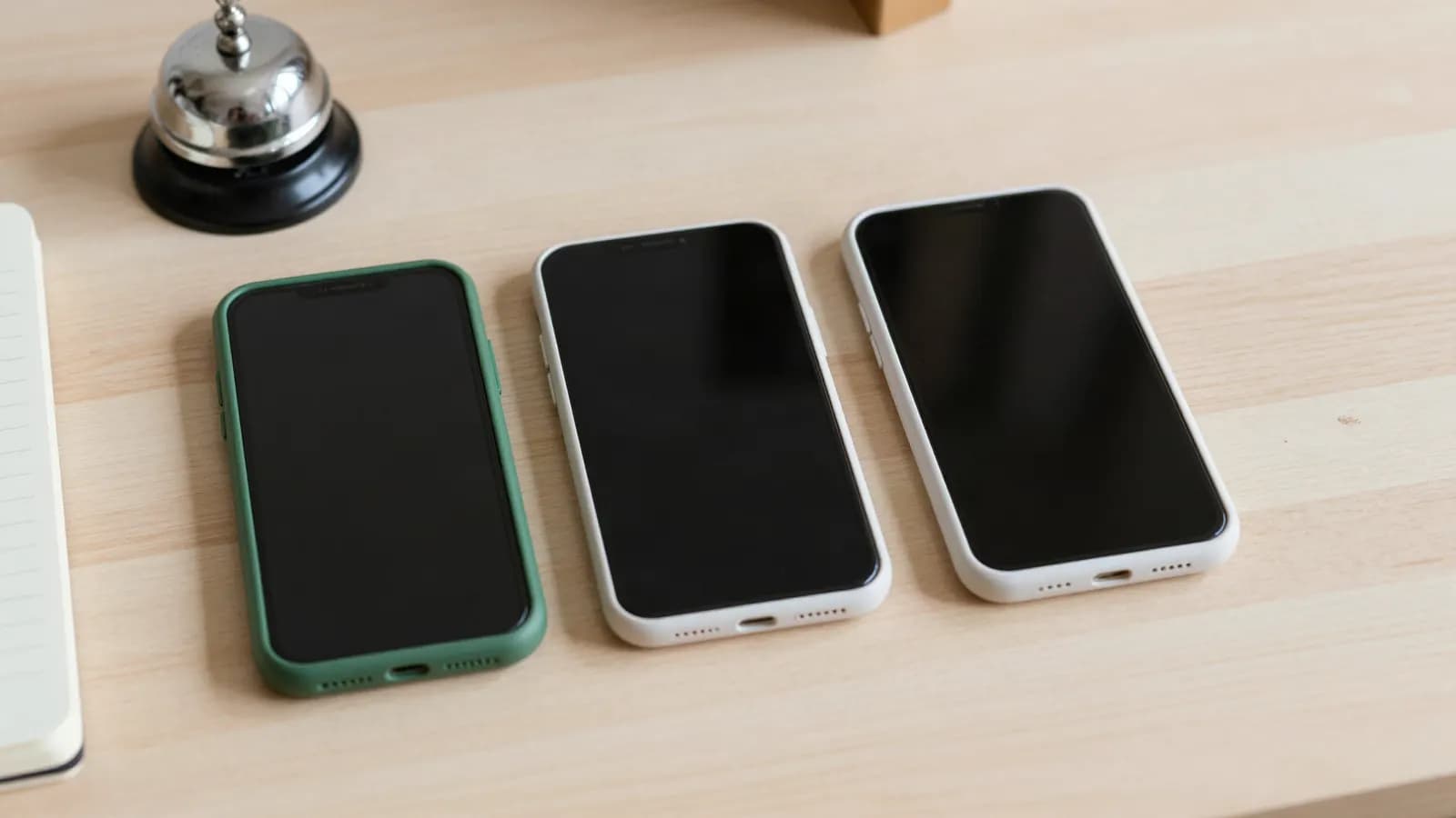 Three smartphones lying side by side on a wooden counter, with a shop service bell behind them