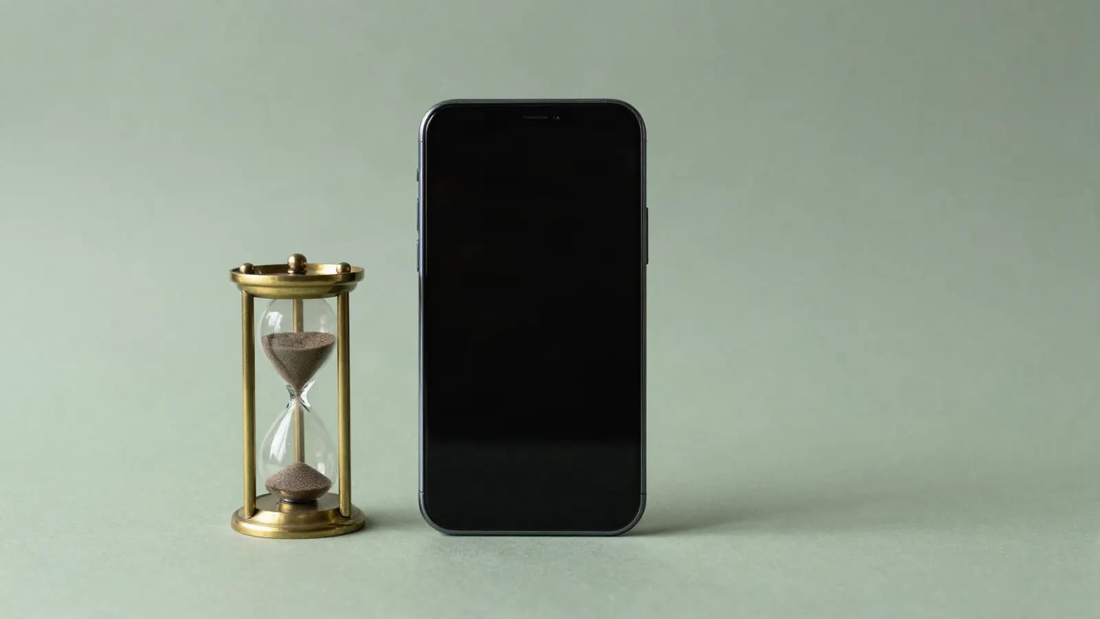 A smartphone lying beside a brass hourglass