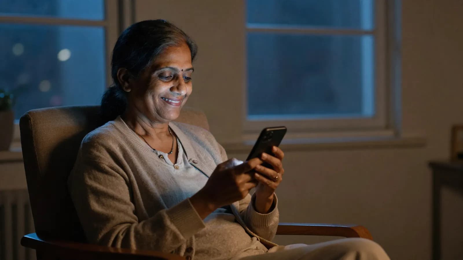 A grandmother at home at night, reading a WhatsApp reply on her phone
