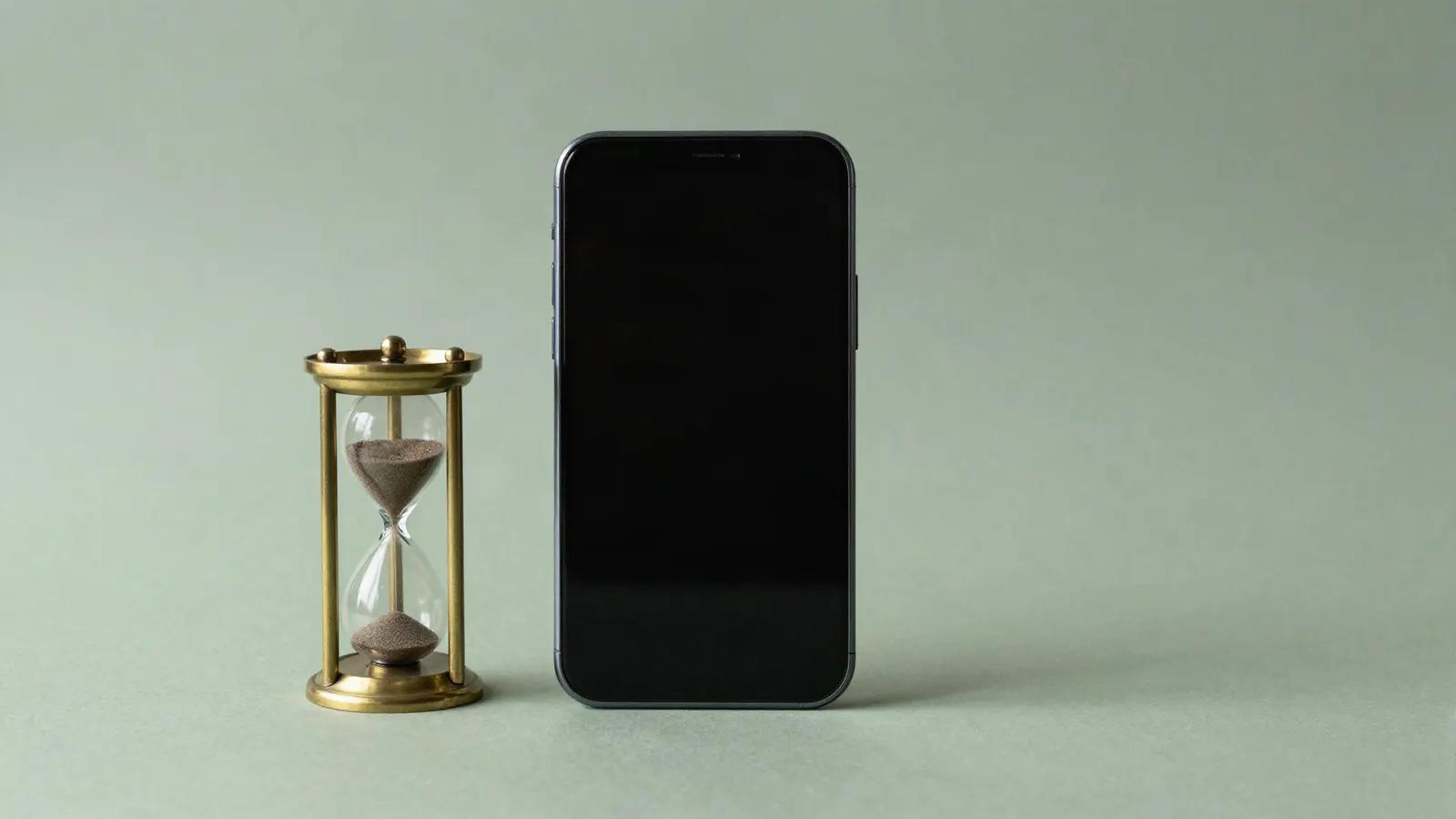 A smartphone lying beside a brass hourglass
